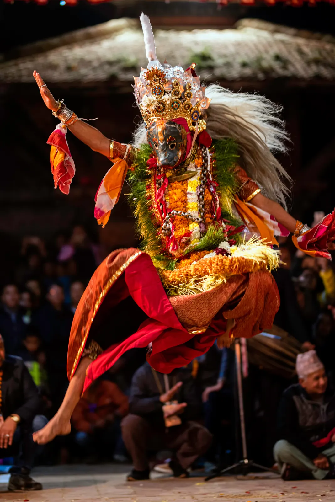 A masked dancer in a silver crown leaps in front of the crowd at Kartik Dabali